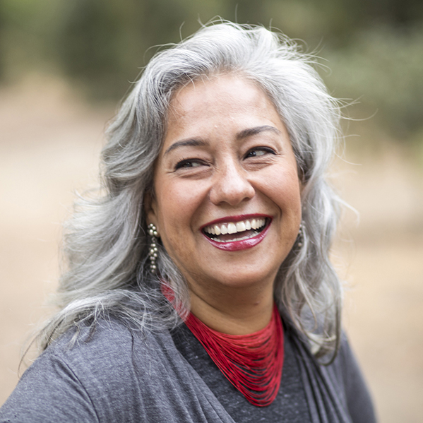A white-haired Mexican woman smiling in nature looking away from camera