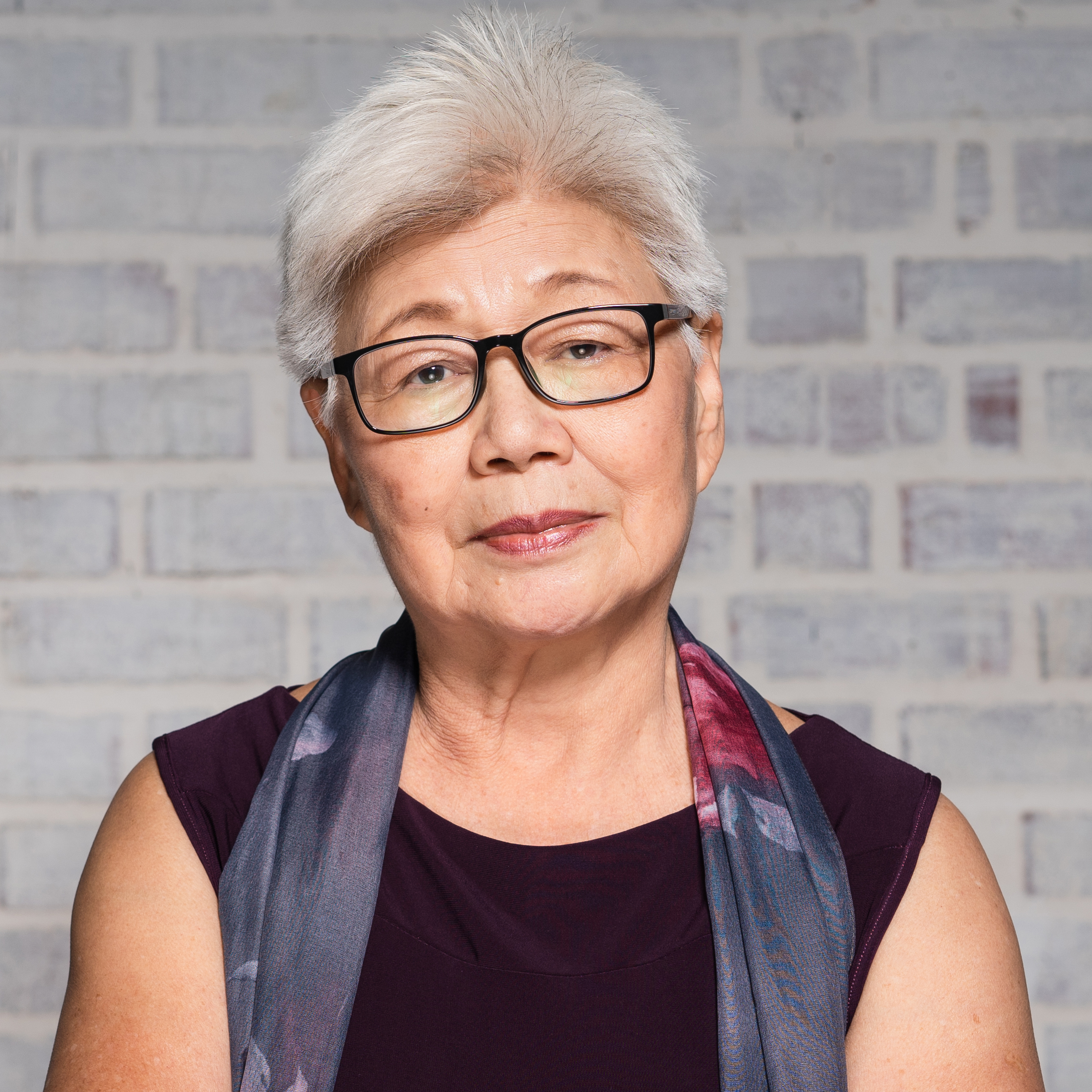 Portrait of Mature Asian Woman staring into camera in front of grey brick wall